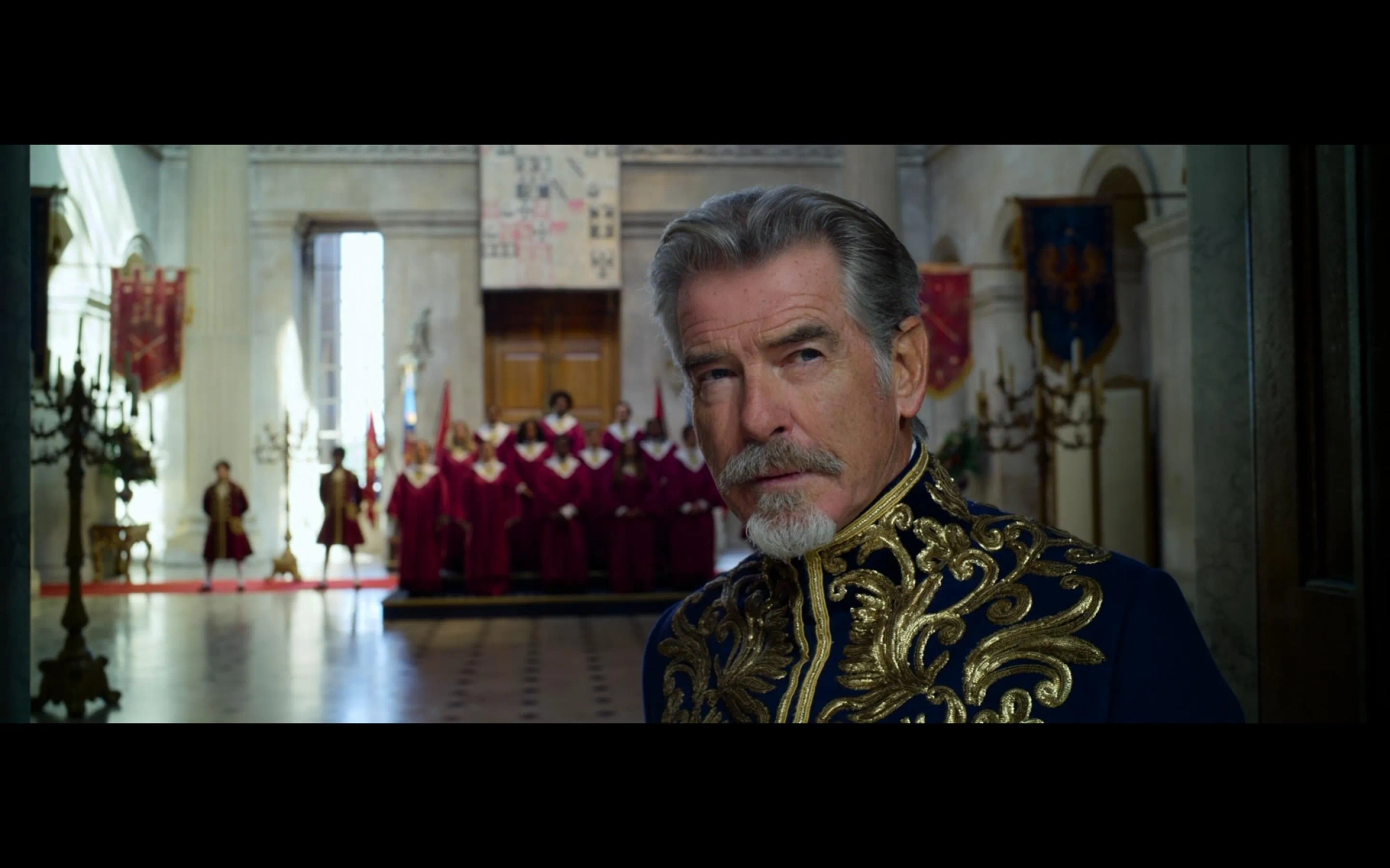 Sanj in the background behind Pierce Brosnan as part of the choir in Cinderella 2021