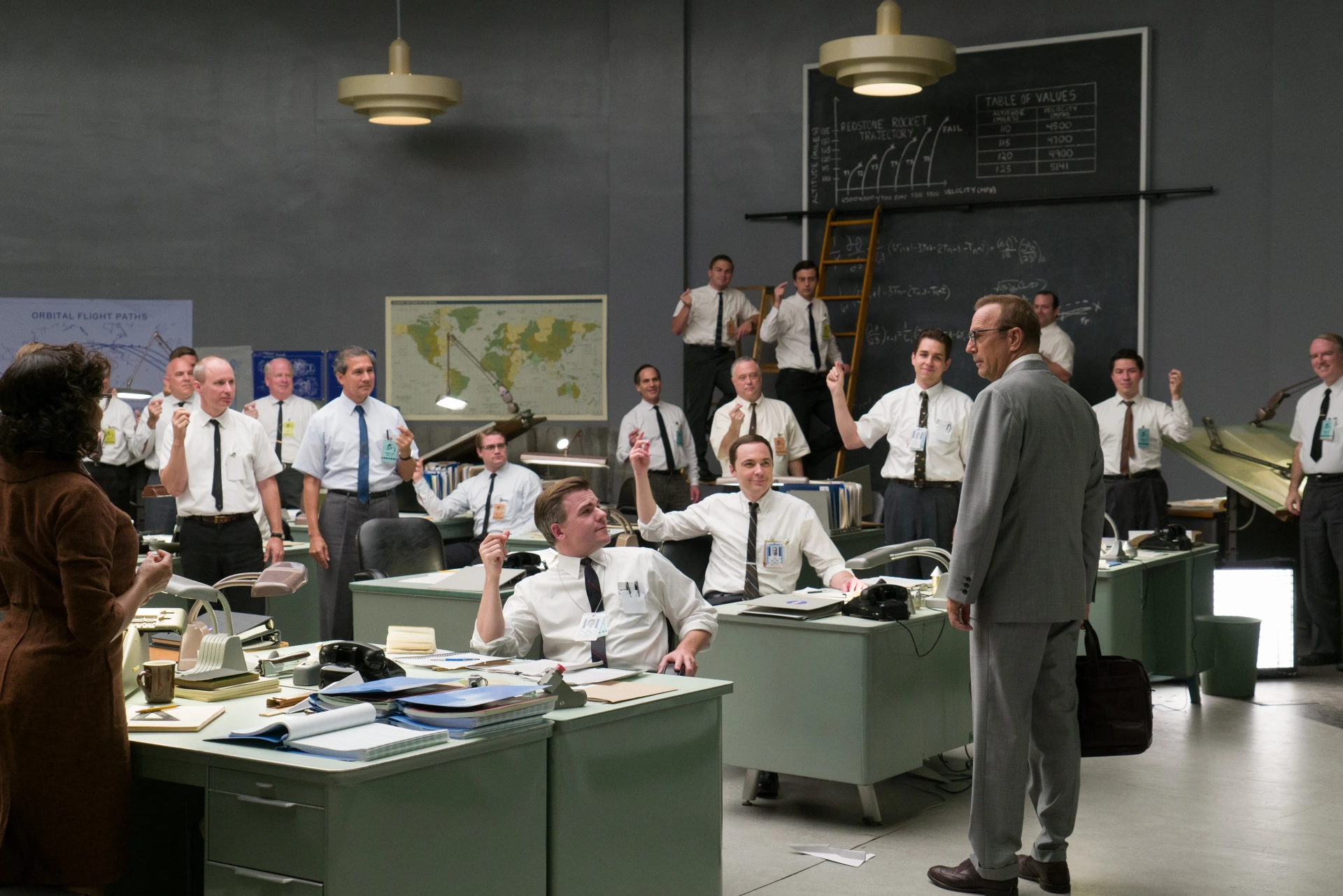 Katherine Johnson (Taraji Henson), Mission Control Commander (Cullen Moss), Paul Stafford (Jim Parsons), Sam Turner (Kurt Krause), and the rest of the Space Task Group give Al Harrison (Kevin Costner) a round of laudatory NASA snaps. From Hidden Figures